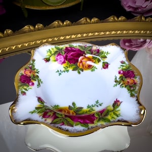 May include: A white porcelain dish with a gold rim and a floral design featuring red, yellow, and pink roses. The dish has a scalloped edge and is ideal for serving snacks or holding jewellery.