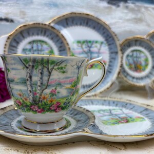 May include: A vintage tea set featuring a cup, saucer, and plates with a landscape design. The cup and plates have a light blue border with gold trim. The cup and plates feature a landscape scene with trees and flowers.