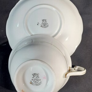 Puede incluir: Taza de t&eacute; y platillo blancos con ribete dorado. La parte inferior de la taza y el platillo tienen un logotipo en blanco y negro que dice "18 R 50 POLEY BONE CHINA MADE IN ENGLAND".