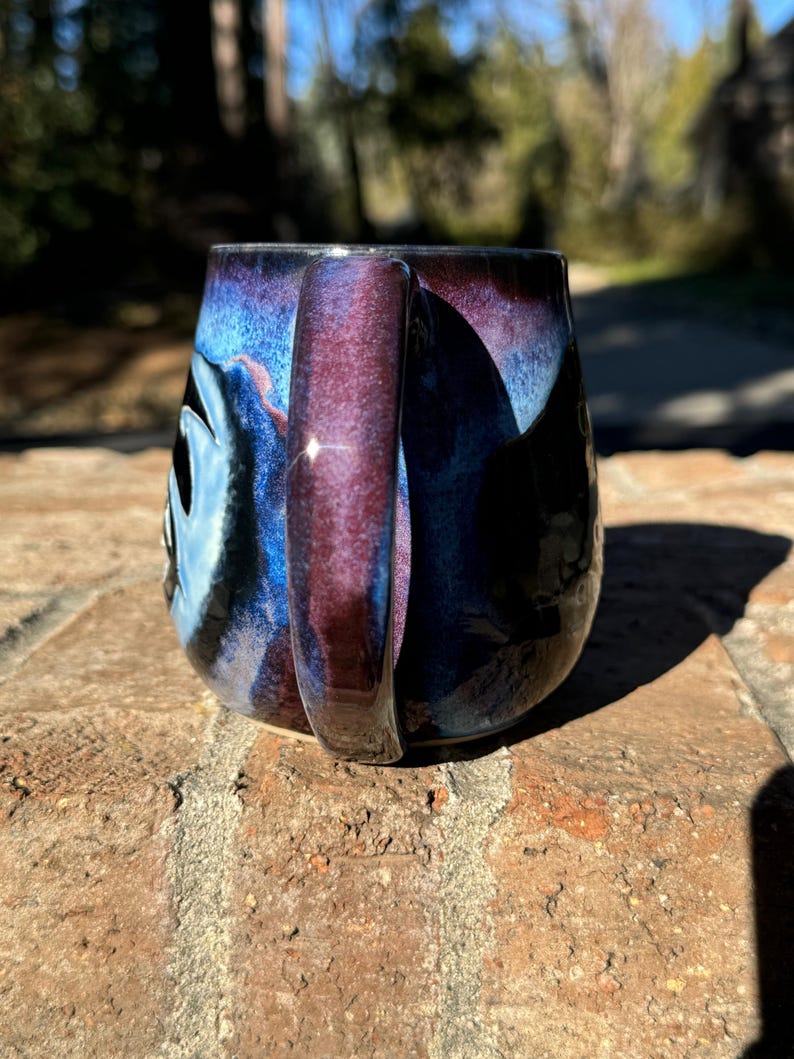 May include: A ceramic mug with a dark blue, purple and black glaze. The mug has a rounded shape and a handle.