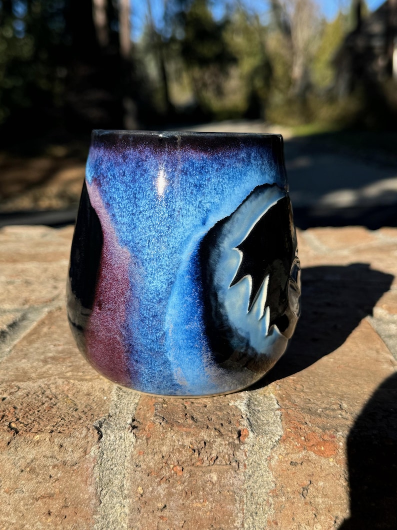 May include: A ceramic mug with a blue, black and purple glaze. The mug has a unique, abstract design.