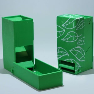 May include: Two green dice towers, one with a white leaf pattern and the other with a plain green finish. Both towers have a compartment for dice and a slot for dice to fall out.