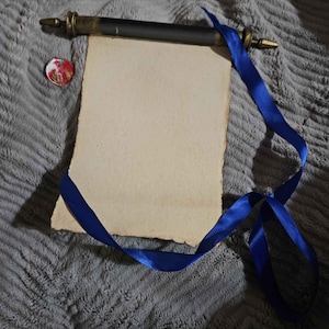 May include: A blank scroll with a blue ribbon tied around it. The scroll is rolled up and tied with a dark brown wooden dowel with brass accents. A red wax seal is attached to the scroll.