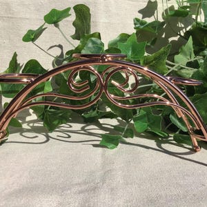 May include: A rose gold metal wine bottle holder with a decorative scroll design. The holder has four rings to hold bottles.
