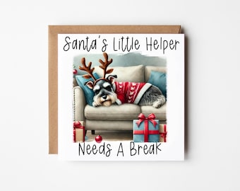May include: A Christmas card featuring a dog wearing a red sweater and reindeer antlers, sleeping on a couch with presents. The card reads "Santa's Little Helper Needs A Break".