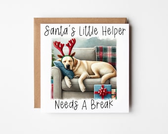 Puede incluir: Una tarjeta de Navidad con un perro blanco que lleva una diadema de reno roja y blanca, durmiendo en un sofá con regalos debajo. La tarjeta dice "Santa's Little Helper Needs A Break".