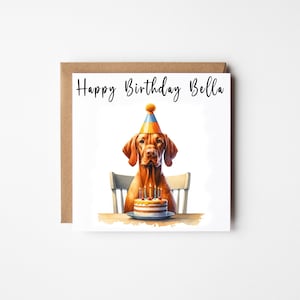 May include: A birthday card featuring a watercolour illustration of a dog wearing a party hat and sitting at a table with a birthday cake. The card says "Happy Birthday Bella".