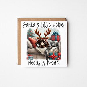 May include: A Christmas card featuring a cartoon illustration of a dog wearing a reindeer antler headband and sleeping on a sofa surrounded by presents. The text on the card reads "Santa's Little Helper Needs A Break".