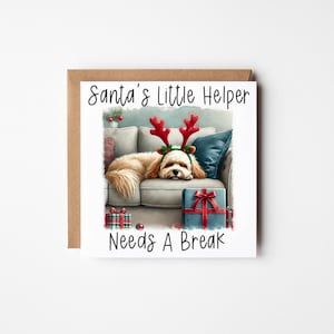 May include: A Christmas card featuring a white dog wearing reindeer antlers, lying on a sofa with presents. The card reads "Santa's Little Helper Needs A Break".