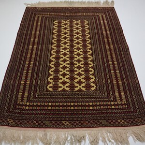 May include: A traditional prayer rug with a red background and intricate geometric patterns in gold and cream. The rug has a fringe border.