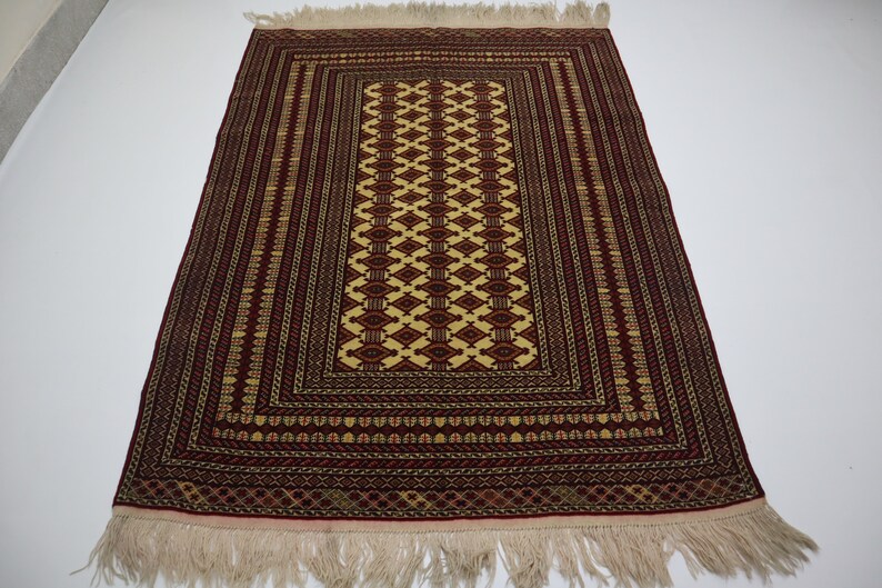 May include: A traditional prayer rug with a red background and intricate geometric patterns in gold and cream. The rug has a fringe border.