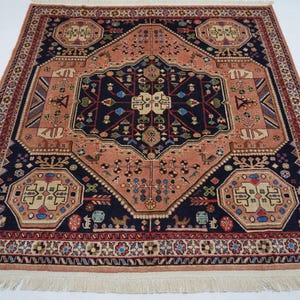 May include: A traditional Persian rug with a central medallion in shades of pink, blue, and black. The rug has a geometric pattern with intricate details and a fringe border.