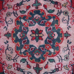 May include: A close-up of a red, pink and blue patterned rug with a floral design. The rug has a central medallion with a starburst pattern.