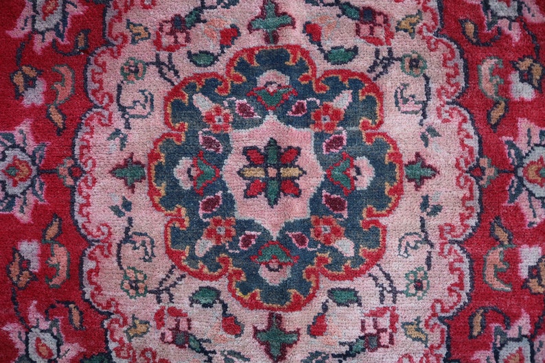 May include: A close-up of a red, pink and blue patterned rug with a floral design. The rug has a central medallion with a starburst pattern.