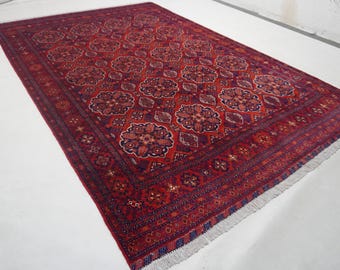 Puede incluir: Una alfombra rectangular anudada a mano con un fondo rojo intenso y intrincados diseños florales en tonos burdeos, azul marino y crema. La alfombra presenta un borde detallado y bordes con flecos, mostrando la artesanía tradicional. Medidas: 200 cm x 300 cm.