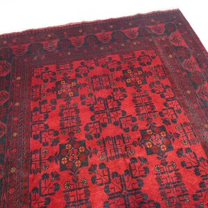 May include: A red rug with a black and white geometric pattern. The rug has a border with a floral design.