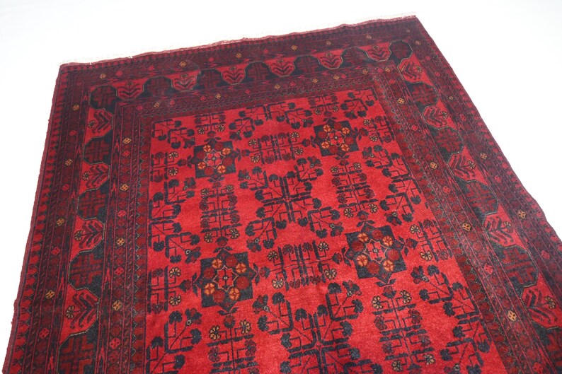 May include: A red rug with a black and white geometric pattern. The rug has a border with a floral design.
