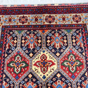 May include: A traditional Persian rug with a navy blue background and intricate geometric patterns in shades of red, green, yellow, and blue. The rug has a fringed border.