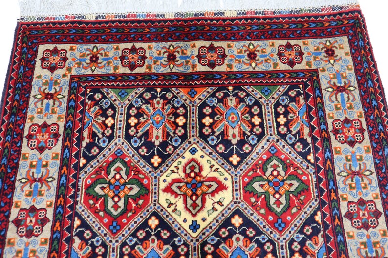 May include: A traditional Persian rug with a navy blue background and intricate geometric patterns in shades of red, green, yellow, and blue. The rug has a fringed border.