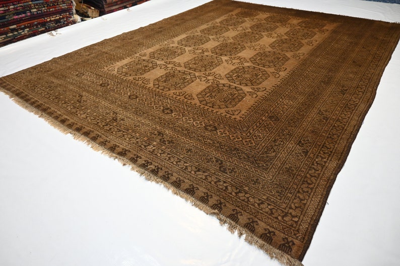 K&ouml;nnte beinhalten: Ein brauner und schwarzer Teppich mit Muster und Fransen. Der Teppich hat ein geometrisches Design mit filigranen Details.