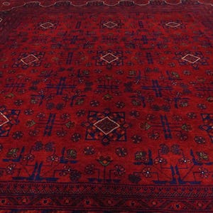 Pu&ograve; includere: Un tappeto rosso con un motivo geometrico in blu e bianco. Il tappeto ha un bordo con un motivo ripetitivo.