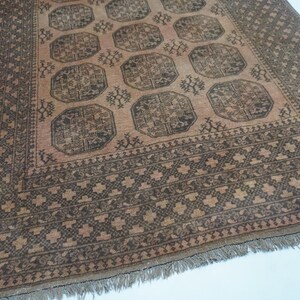 May include: A rectangular, hand-woven rug with a central field of peach and dark brown geometric patterns. The rug features a repeating octagonal design and a detailed border. Fringes are visible along the bottom edge.
