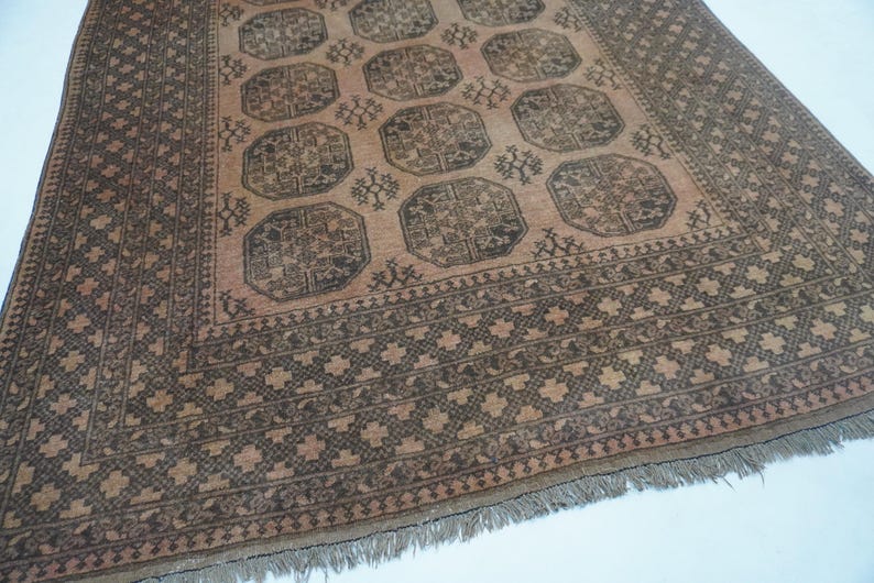 May include: A rectangular, hand-woven rug with a central field of peach and dark brown geometric patterns. The rug features a repeating octagonal design and a detailed border. Fringes are visible along the bottom edge.