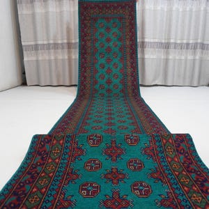 May include: A long, narrow runner rug featuring a vibrant teal background with a repeating geometric pattern in shades of red, dark blue, and green. The rug has a detailed border with intricate diamond and cross motifs running along the edges.