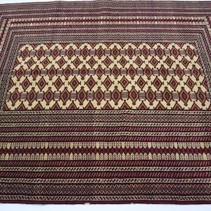 May include: A traditional Persian rug with a red background and intricate geometric patterns in shades of cream, red, and blue. The rug has a fringe border.