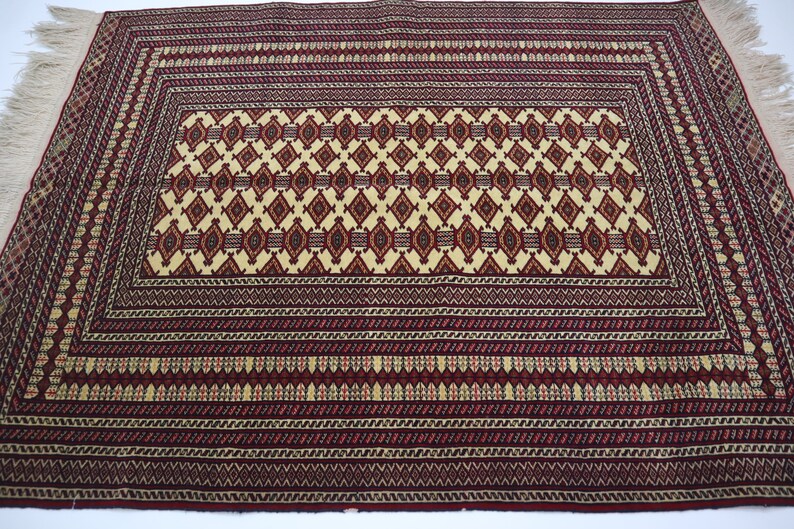 May include: A traditional Persian rug with a red background and intricate geometric patterns in shades of cream, red, and blue. The rug has a fringe border.