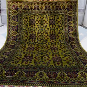 May include: A green and burgundy rug with a geometric pattern. The rug has a central square with a repeating design of stylized flowers and leaves.