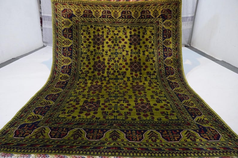 May include: A green and burgundy rug with a geometric pattern. The rug has a central square with a repeating design of stylized flowers and leaves.