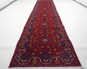Könnte beinhalten: Ein langer, rechteckiger roter Teppich mit komplizierten Mustern in Blau, Gelb und Weiß. Der Teppich hat ein zentrales Design mit floralen Motiven und einen detaillierten Rand. Der Teppich hat an beiden Enden einen Fransen.