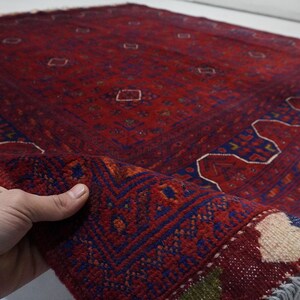 Pu&ograve; includere: Un tappeto rosso, blu e bianco con un bordo a frangia. Il tappeto presenta un design tradizionale con forme geometriche e motivi floreali.