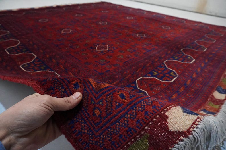 Pu&ograve; includere: Un tappeto rosso, blu e bianco con un bordo a frangia. Il tappeto presenta un design tradizionale con forme geometriche e motivi floreali.