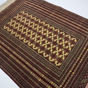 May include: A traditional rug with a red, cream, and brown geometric pattern. The rug has a fringe border.