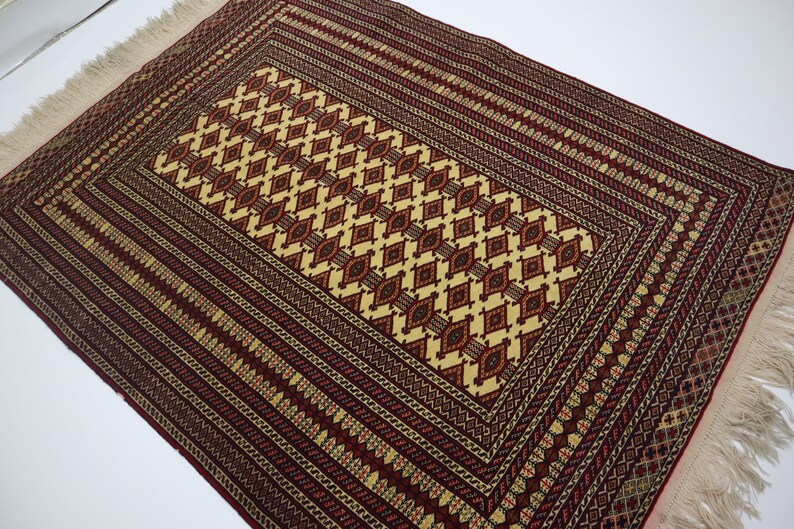 May include: A traditional rug with a red, cream, and brown geometric pattern. The rug has a fringe border.