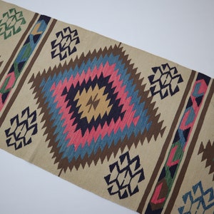 May include: Beige runner rug with geometric diamond patterns in shades of pink, blue, brown, green, and yellow. The rug features a repeating design of diamond shapes and stylized geometric motifs.