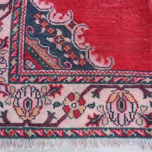 May include: Close-up of a red rug with a detailed floral border. The border is a mix of pink, blue, green, and white.