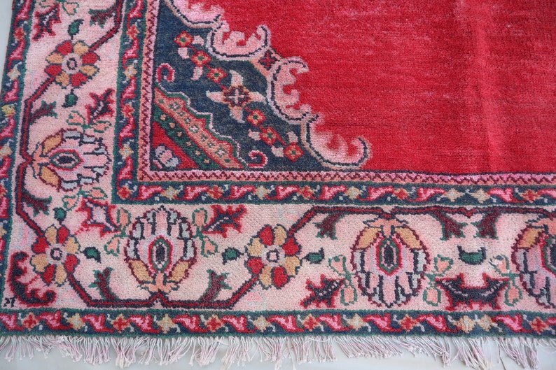 May include: Close-up of a red rug with a detailed floral border. The border is a mix of pink, blue, green, and white.