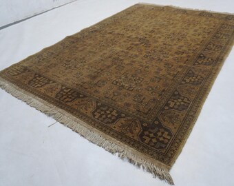 May include: A rectangular, hand-woven rug with a warm, earthy color palette. The rug features a central field with a repeating pattern and a detailed border in shades of brown and tan. Fringes are visible along the shorter edges.