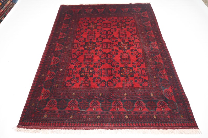 May include: A red and black patterned rug with a detailed geometric design. The rug has a fringe border.