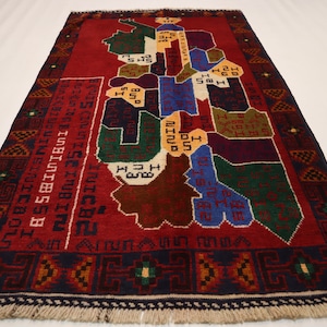 Puede incluir: Una alfombra roja, azul, verde y blanca con un diseño geométrico. La alfombra tiene un borde de flecos y presenta texto en un idioma extranjero.