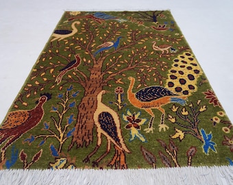 May include: A rectangular green rug with a tree and bird design. The rug features a central tree with brown branches and various birds in shades of brown, blue, and yellow. The rug has a fringe along the bottom edge.