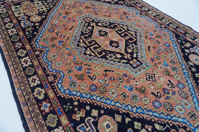 May include: A vintage rug with a central medallion design in shades of pink, blue, and black. The rug features intricate floral patterns and geometric motifs.