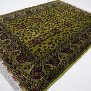 May include: A green rug with a traditional Persian design. The rug has a dark blue border with red and white accents. The center of the rug is a light green color with a repeating pattern of flowers and leaves.