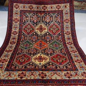 May include: A traditional Persian rug with a geometric pattern in shades of red, blue, green, and cream. The rug has a central medallion and a border with intricate floral designs.