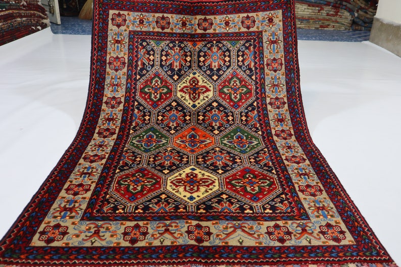 May include: A traditional Persian rug with a geometric pattern in shades of red, blue, green, and cream. The rug has a central medallion and a border with intricate floral designs.