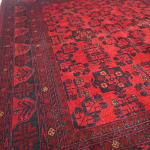 May include: A red and black patterned rug with a traditional design. The rug has a dark border with intricate details and a central field with repeating motifs.