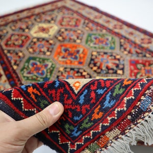 May include: A colourful hand-woven rug with a geometric pattern in shades of red, blue, green, and yellow. The rug has a fringe border and is folded in half.